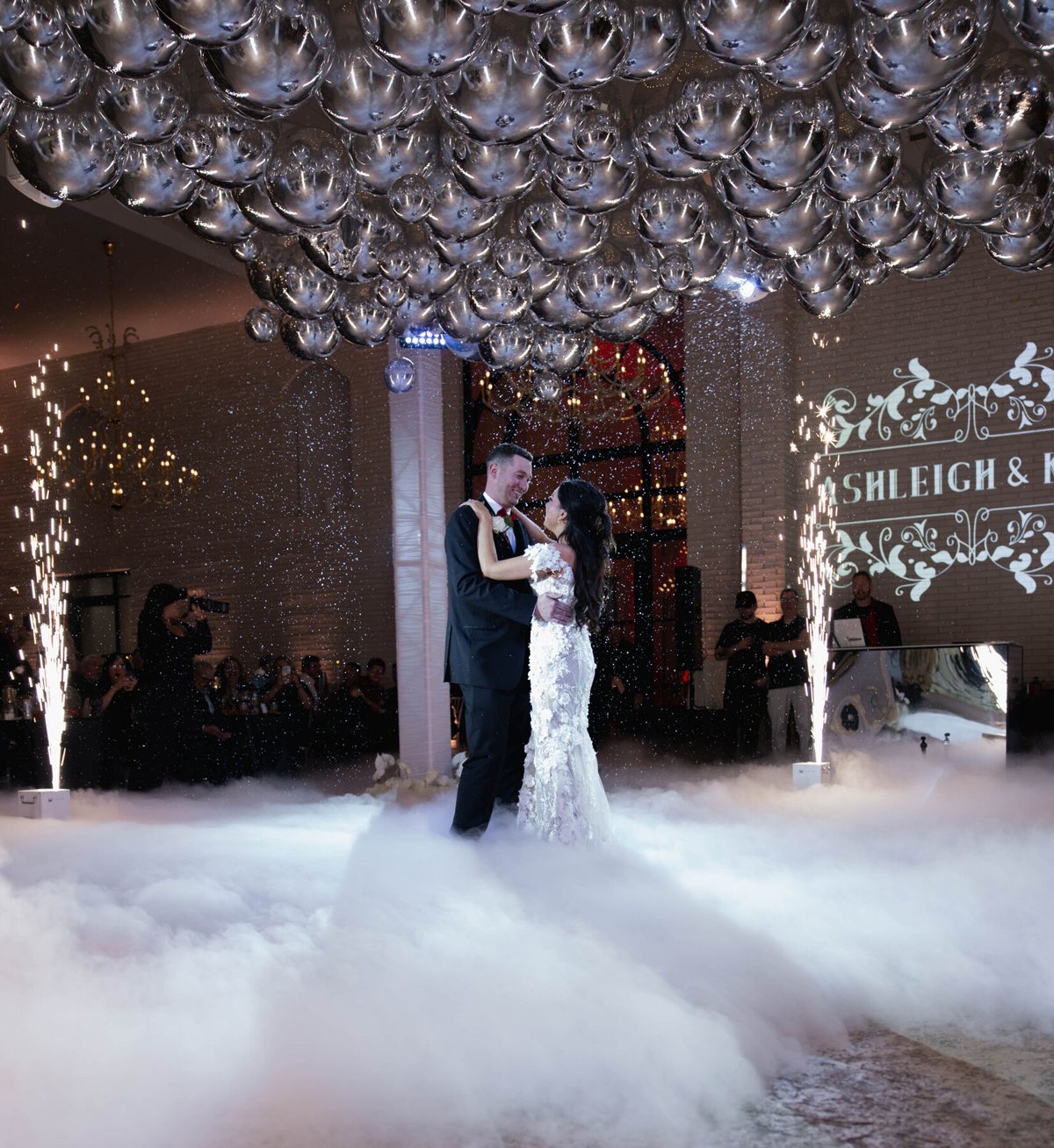Couple's first dance on a cloud of fog under a silver balloon ceiling with sparkler fountains